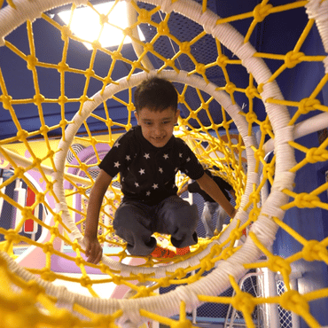 Child climbing through a colourful rope tunnel at Wooray Patna indoor play area.