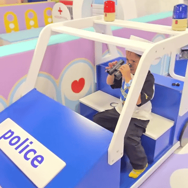 Child enjoying a police-themed pretend play activity inside a toy police vehicle at Wooray Patna.